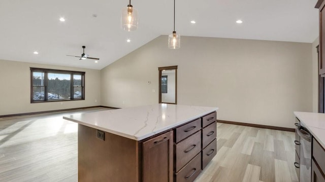 kitchen with light stone counters, light wood-style floors, open floor plan, vaulted ceiling, and decorative light fixtures