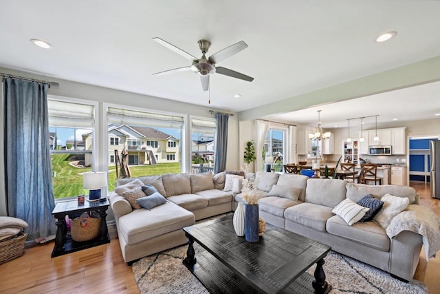 living room with ceiling fan with notable chandelier and light hardwood / wood-style floors