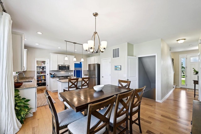 dining space with light hardwood / wood-style flooring, an inviting chandelier, and sink