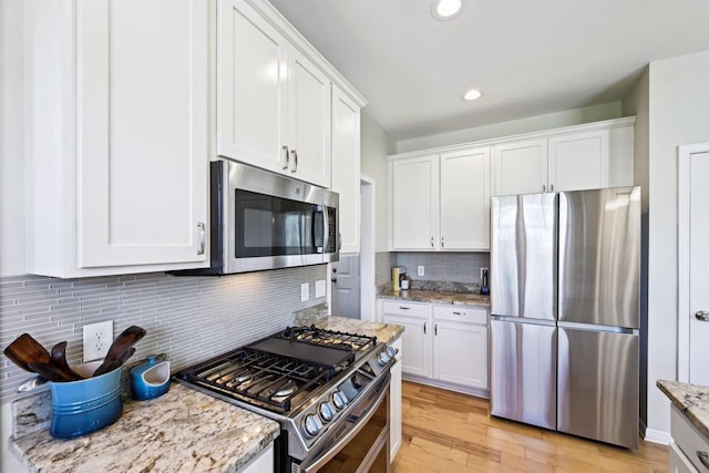 kitchen featuring light stone countertops, white cabinetry, tasteful backsplash, light hardwood / wood-style floors, and appliances with stainless steel finishes