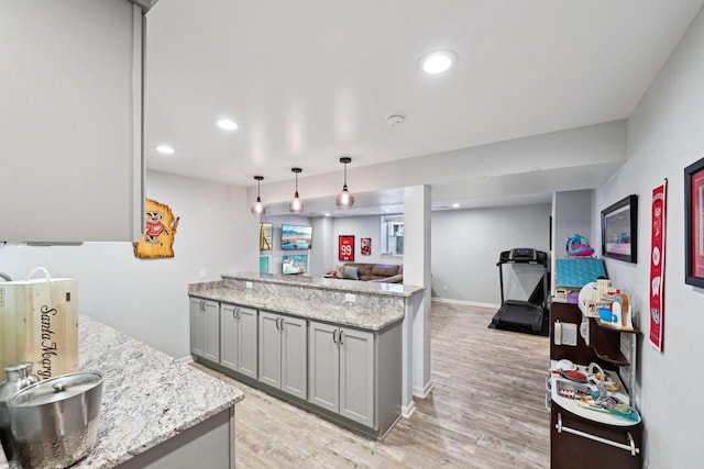 kitchen with pendant lighting, light wood-type flooring, light stone counters, and gray cabinetry