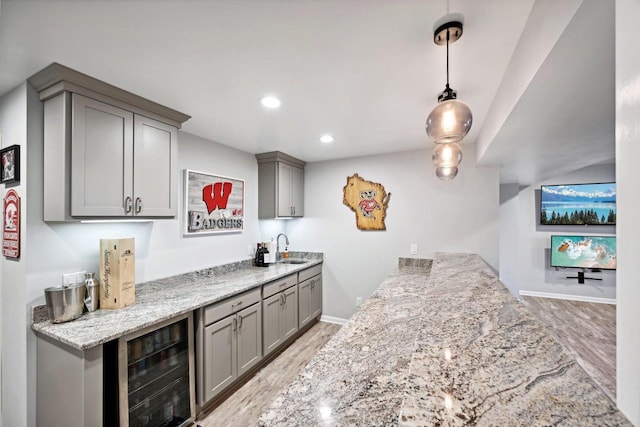 bar with sink, hanging light fixtures, wine cooler, light stone counters, and light hardwood / wood-style floors