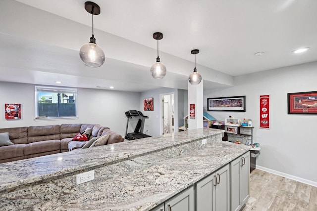 kitchen with light stone counters, decorative light fixtures, and light wood-type flooring