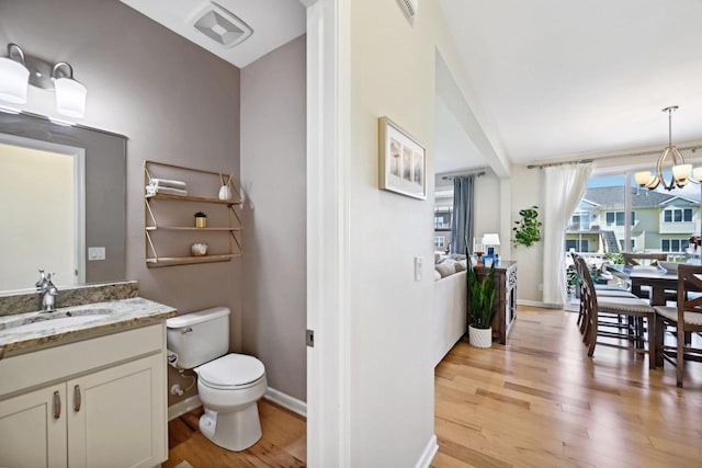 bathroom with hardwood / wood-style floors, vanity, toilet, and an inviting chandelier