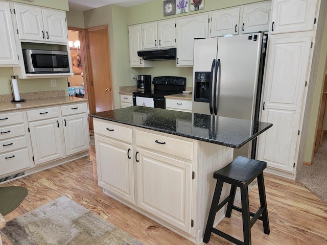 kitchen featuring dark stone counters, stainless steel appliances, light hardwood / wood-style flooring, white cabinets, and a center island