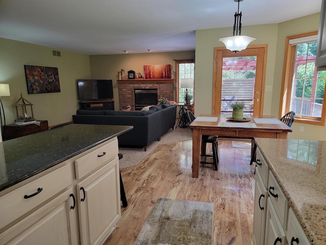 kitchen with light stone counters, a fireplace, white cabinets, and pendant lighting