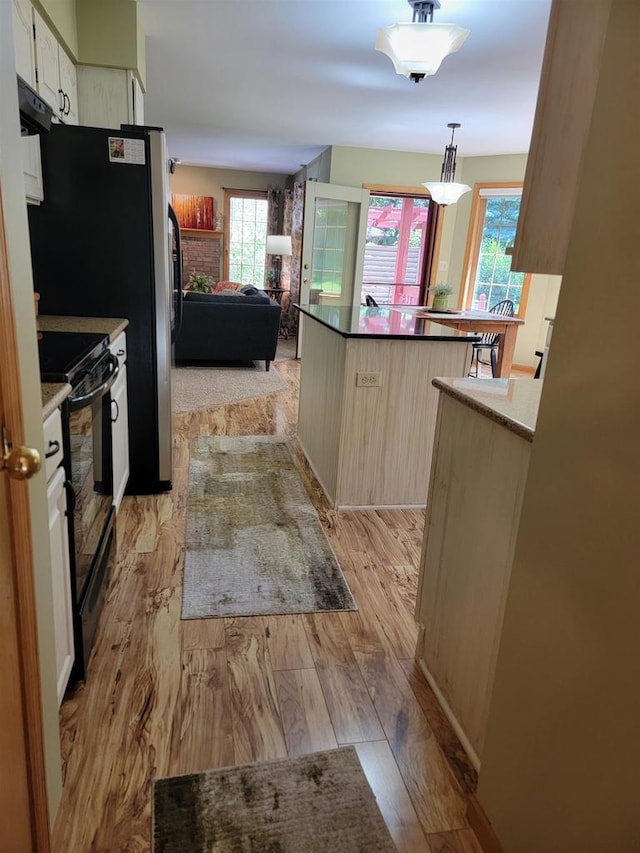 kitchen featuring black electric range oven, hanging light fixtures, and light hardwood / wood-style flooring