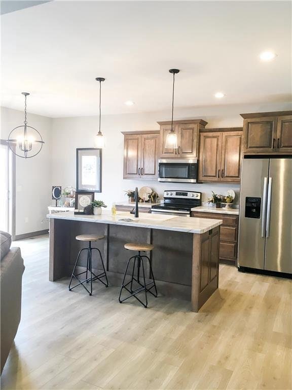 kitchen featuring a chandelier, light wood-type flooring, stainless steel appliances, and a center island with sink