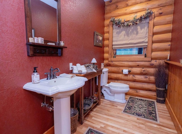 bathroom with toilet, wood-type flooring, and rustic walls