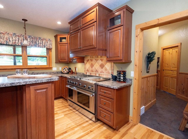 kitchen featuring double oven range, wooden walls, light hardwood / wood-style flooring, tasteful backsplash, and decorative light fixtures