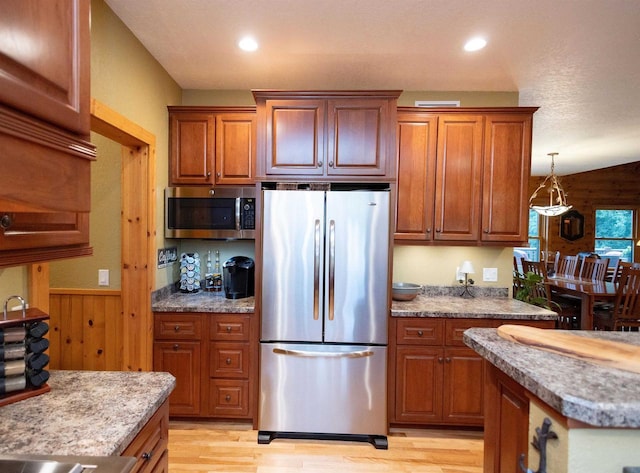 kitchen with appliances with stainless steel finishes, a textured ceiling, wooden walls, light hardwood / wood-style flooring, and lofted ceiling