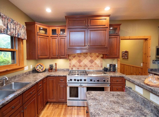 kitchen featuring range with two ovens, sink, light wood-type flooring, tasteful backsplash, and light stone counters