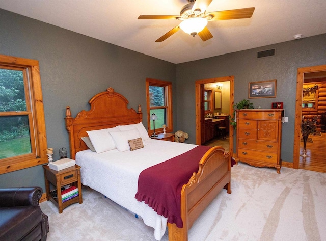 bedroom with ceiling fan, light colored carpet, and connected bathroom