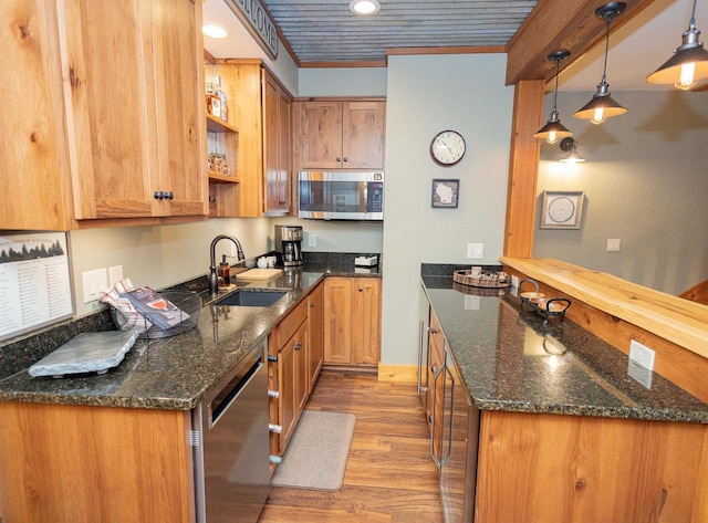 kitchen with dark stone counters, stainless steel appliances, sink, decorative light fixtures, and hardwood / wood-style floors