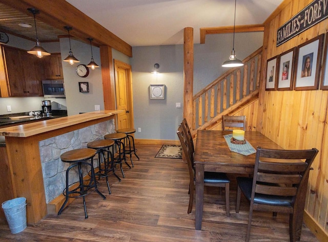 dining area with wooden walls, beamed ceiling, and dark wood-type flooring