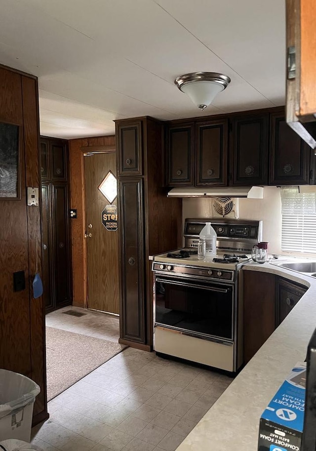 kitchen with dark brown cabinets, wooden walls, and gas range