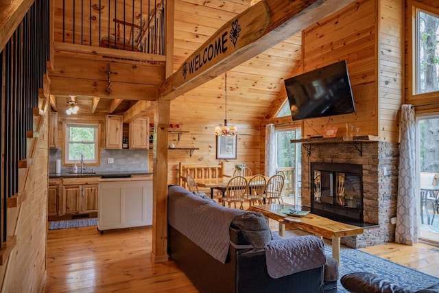 living room with sink, wooden walls, a fireplace, ceiling fan with notable chandelier, and light wood-type flooring