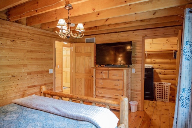 bedroom featuring beam ceiling, wood walls, an inviting chandelier, and light wood-type flooring