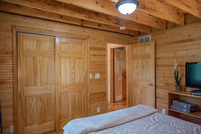 bedroom with beam ceiling, wooden walls, and a closet