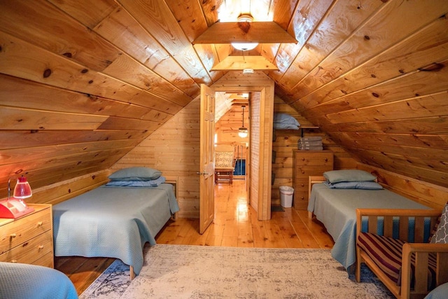 bedroom with wood walls, lofted ceiling, connected bathroom, and light hardwood / wood-style flooring