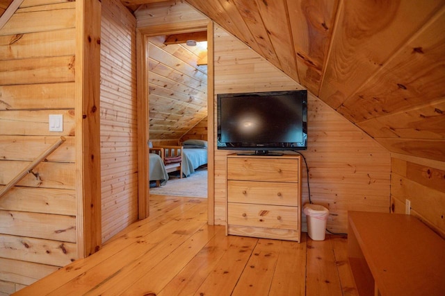 additional living space with light hardwood / wood-style floors, vaulted ceiling, and wooden walls