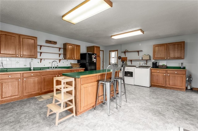 kitchen featuring black refrigerator, a kitchen breakfast bar, a textured ceiling, sink, and washing machine and clothes dryer