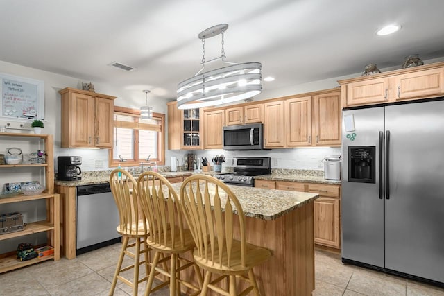 kitchen featuring a kitchen bar, light stone countertops, a center island, and appliances with stainless steel finishes