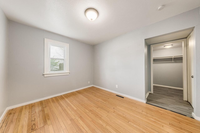 unfurnished bedroom featuring a textured ceiling, a walk in closet, light hardwood / wood-style floors, and a closet