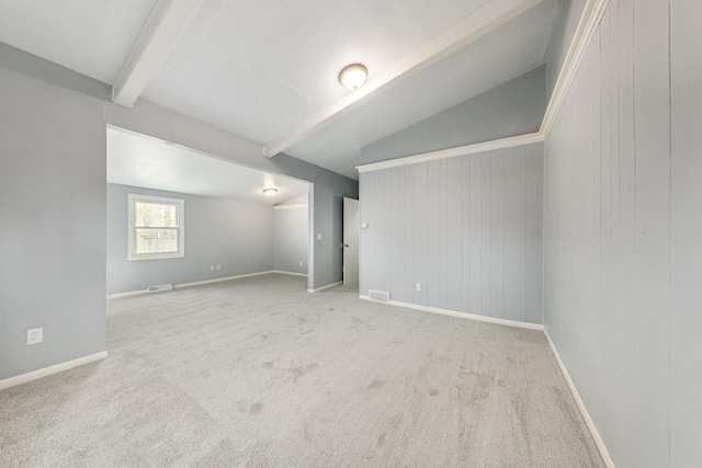 spare room with vaulted ceiling with beams, wood walls, and light colored carpet