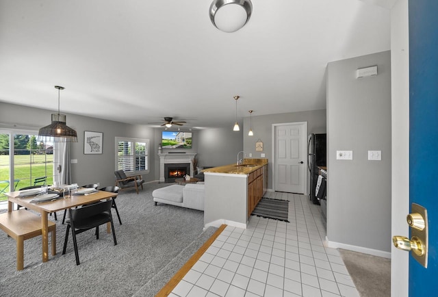 kitchen featuring light carpet, black fridge, hanging light fixtures, sink, and ceiling fan