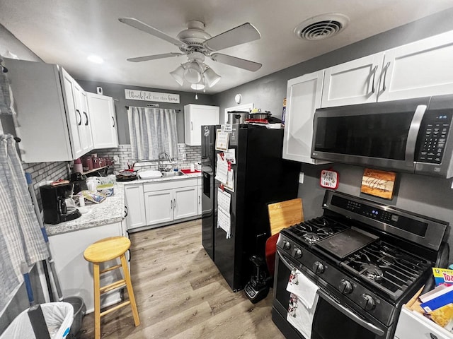 kitchen with black appliances, sink, light hardwood / wood-style flooring, tasteful backsplash, and white cabinetry