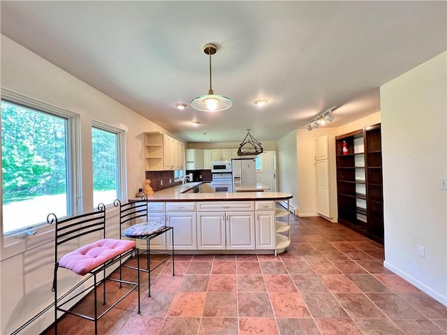 kitchen with kitchen peninsula, track lighting, white appliances, baseboard heating, and hanging light fixtures