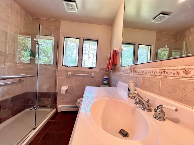 bathroom with tile patterned flooring, a baseboard heating unit, toilet, a shower with shower door, and tile walls