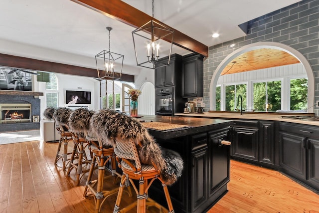 kitchen with a breakfast bar, light hardwood / wood-style flooring, a center island, black oven, and stainless steel gas stovetop