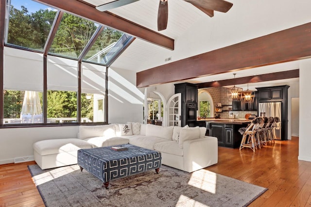 living room with beam ceiling, ceiling fan, light hardwood / wood-style flooring, and high vaulted ceiling