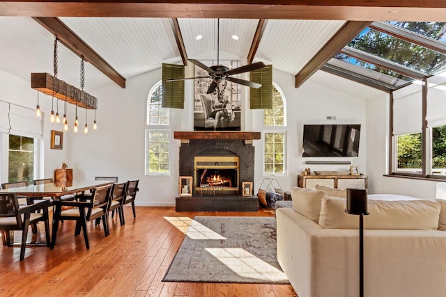 living room with a brick fireplace, ceiling fan, beam ceiling, high vaulted ceiling, and light hardwood / wood-style flooring