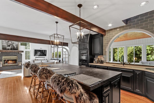 kitchen with sink, a kitchen breakfast bar, light hardwood / wood-style flooring, black double oven, and a kitchen island