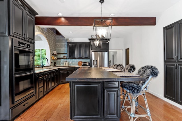 kitchen with beamed ceiling, appliances with stainless steel finishes, light hardwood / wood-style floors, and a kitchen island