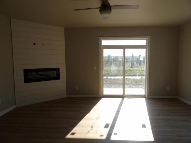 unfurnished living room featuring a large fireplace, ceiling fan, and dark hardwood / wood-style flooring