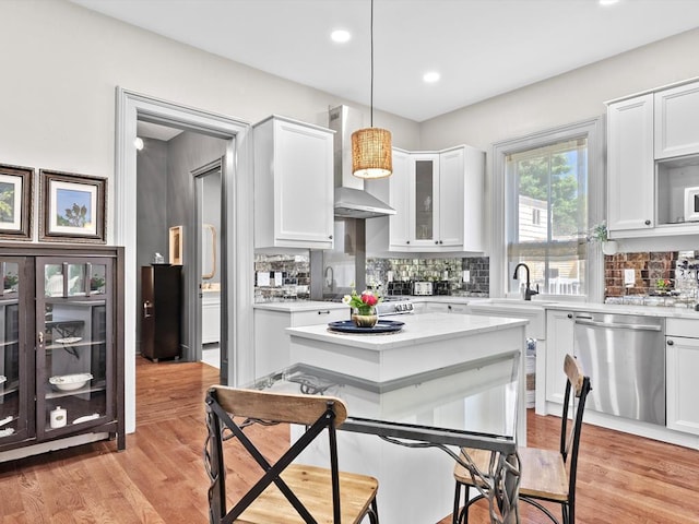 kitchen featuring white cabinetry, wall chimney exhaust hood, hanging light fixtures, stainless steel dishwasher, and backsplash