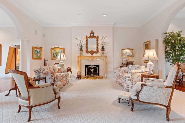 living area with a fireplace, light hardwood / wood-style flooring, crown molding, and ornate columns