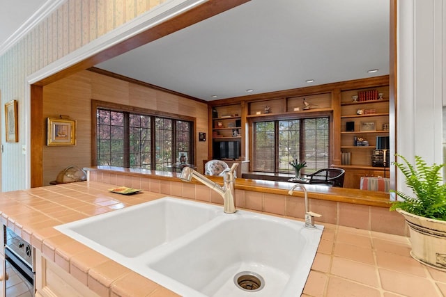 kitchen featuring tile patterned floors, crown molding, sink, built in features, and tile counters