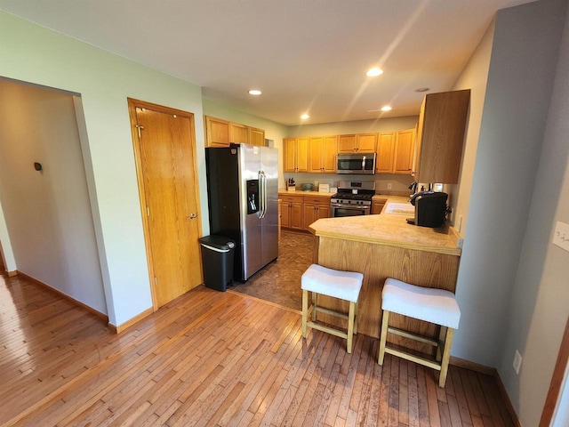 kitchen with a kitchen breakfast bar, kitchen peninsula, light hardwood / wood-style flooring, and appliances with stainless steel finishes