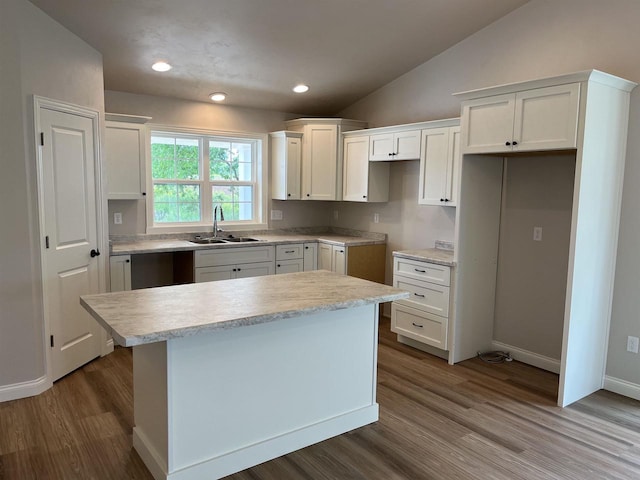 kitchen featuring a center island, white cabinets, sink, vaulted ceiling, and wood-type flooring