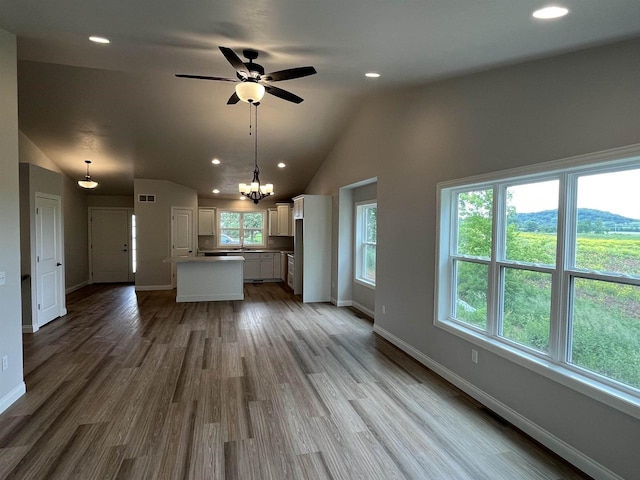 unfurnished living room featuring ceiling fan with notable chandelier, lofted ceiling, sink, and light hardwood / wood-style flooring