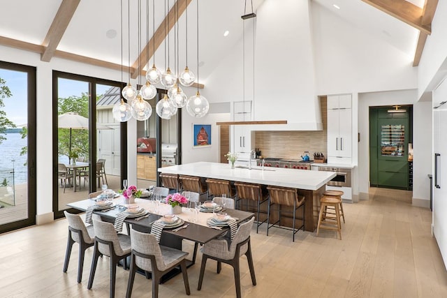 dining area with beamed ceiling, high vaulted ceiling, sink, and light hardwood / wood-style floors