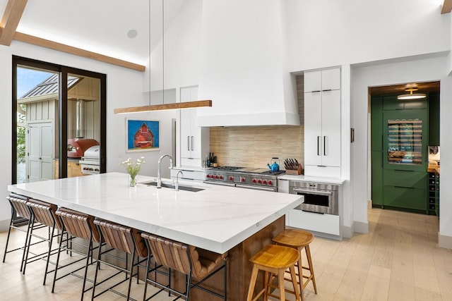 kitchen featuring sink, appliances with stainless steel finishes, a kitchen island with sink, white cabinets, and a kitchen bar