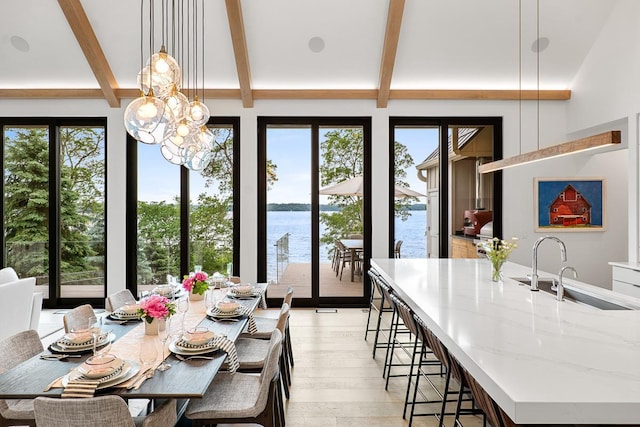 dining space featuring beam ceiling, a water view, sink, and light wood-type flooring