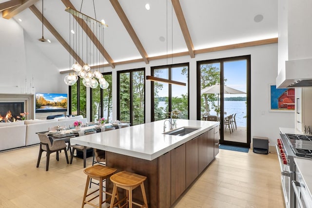 kitchen with beamed ceiling, sink, stainless steel range, a water view, and a center island with sink