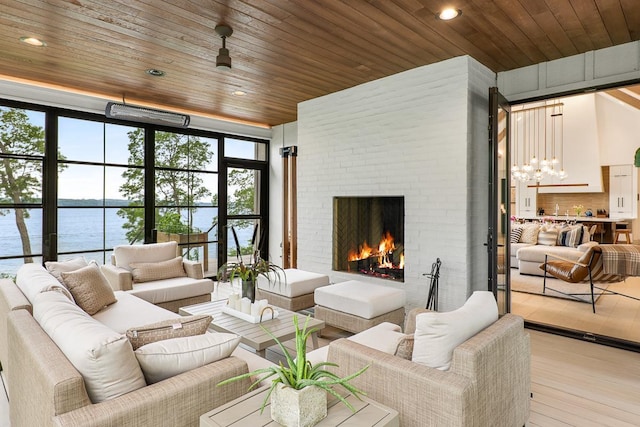 living room featuring a water view, wood ceiling, a brick fireplace, light hardwood / wood-style flooring, and a wall of windows